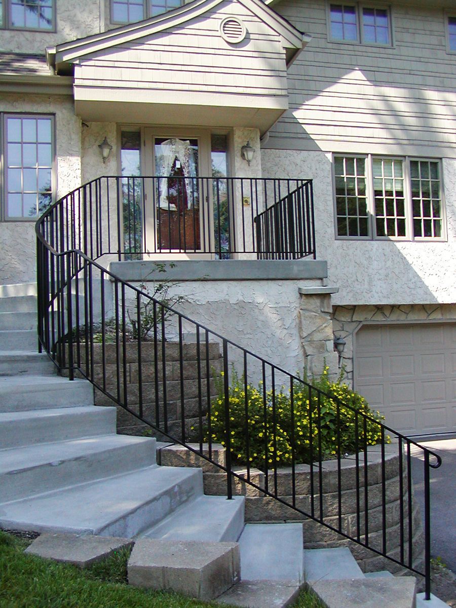 Exterior of a house with concrete steps, black railing, and a small front porch.