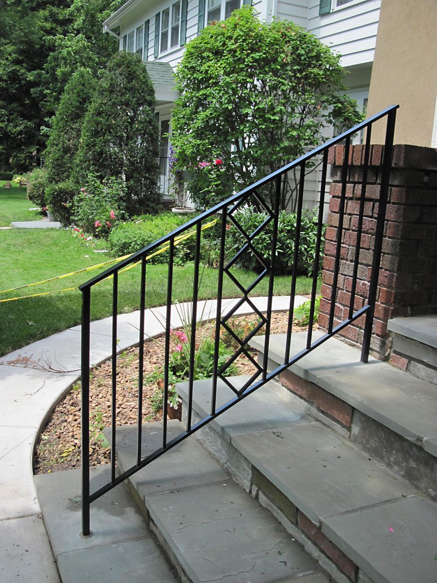 Black wrought-iron railing on steps leading to a house, with green lawn and landscaping.