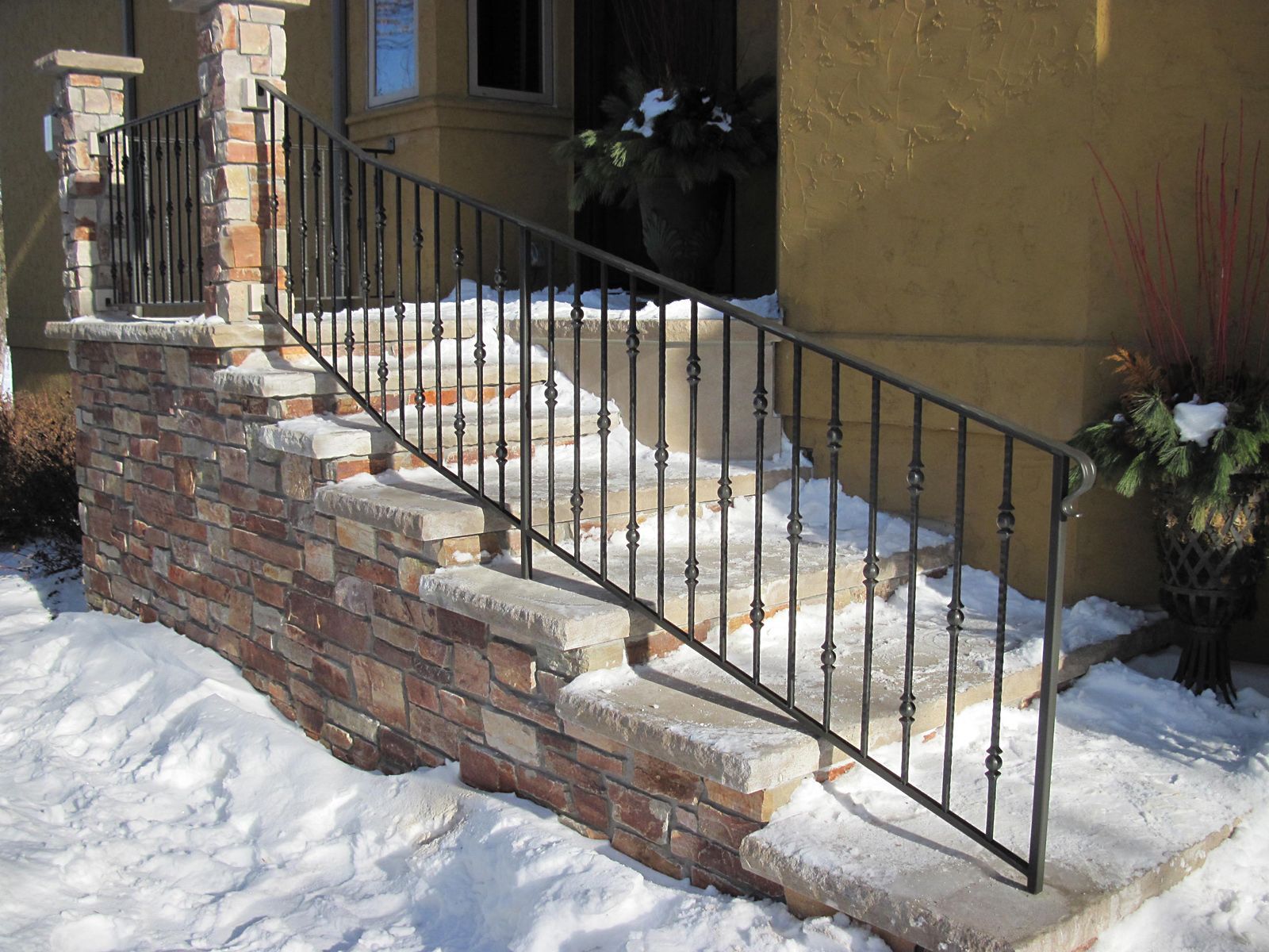 Stone steps with wrought iron railing, leading to a front door, set in a snowy environment.