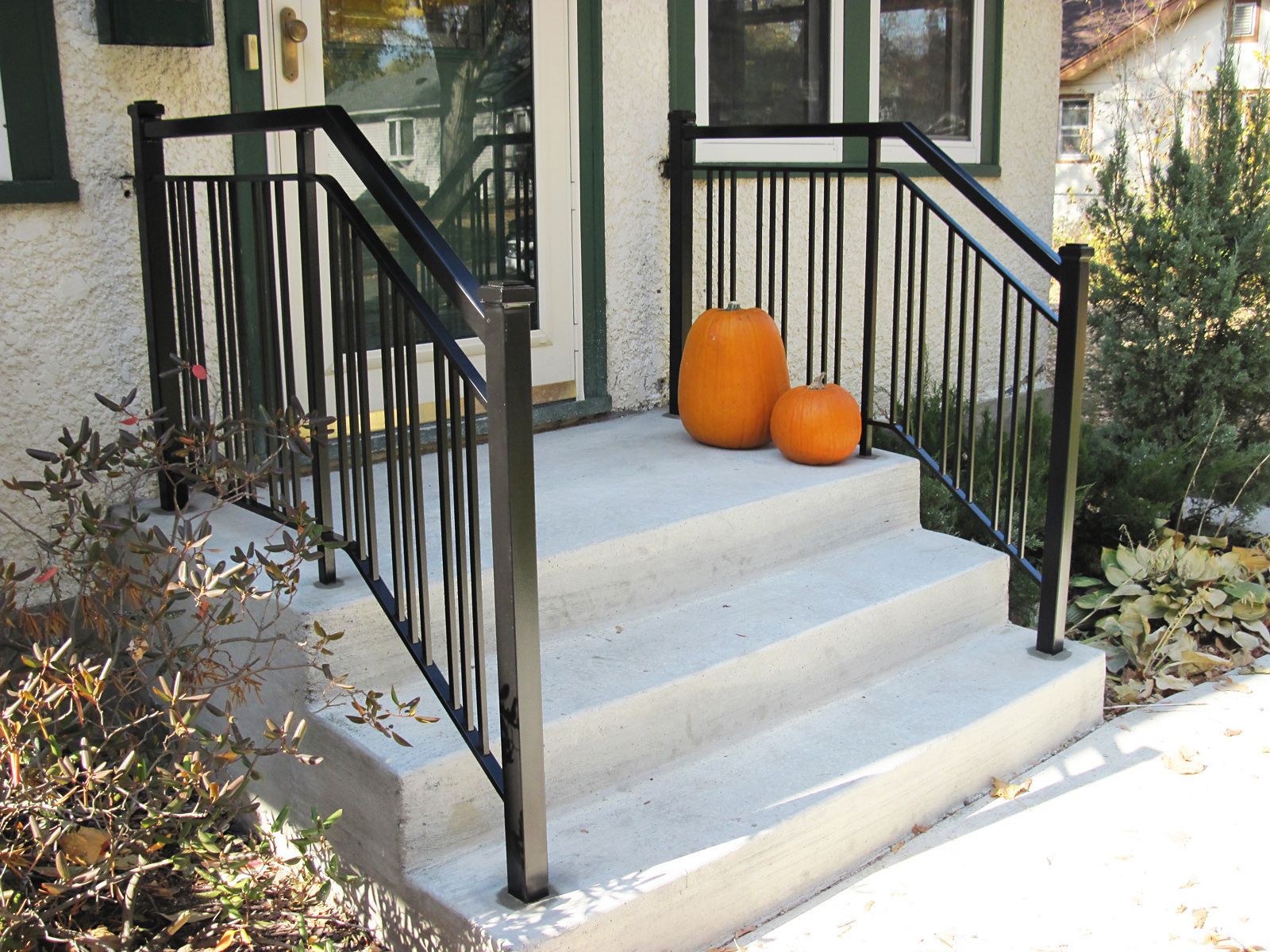Concrete steps leading to a house entrance, black metal railing, two pumpkins.