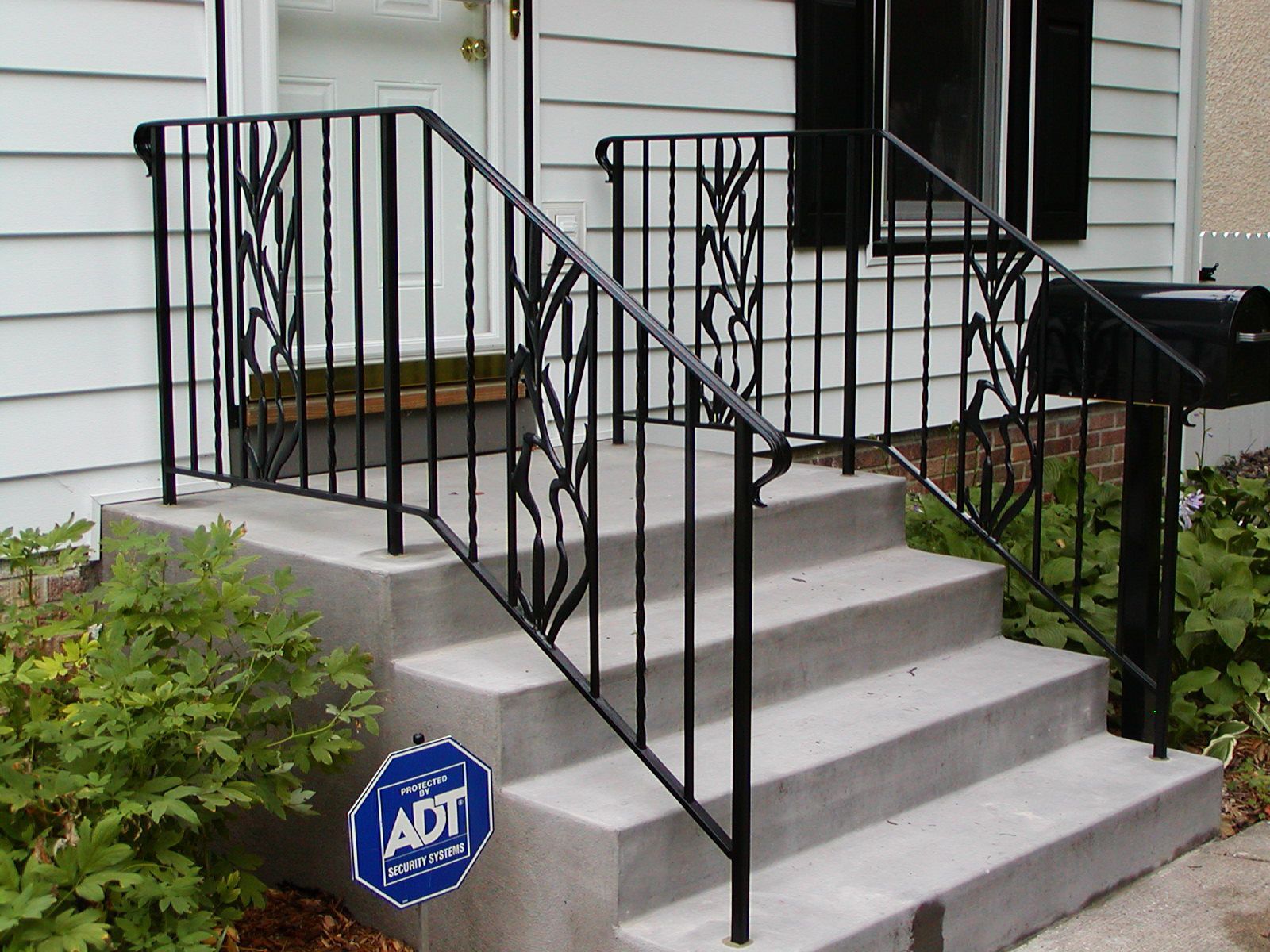 Concrete steps with black wrought-iron railings. A front door is in the background. An ADT sign is visible.