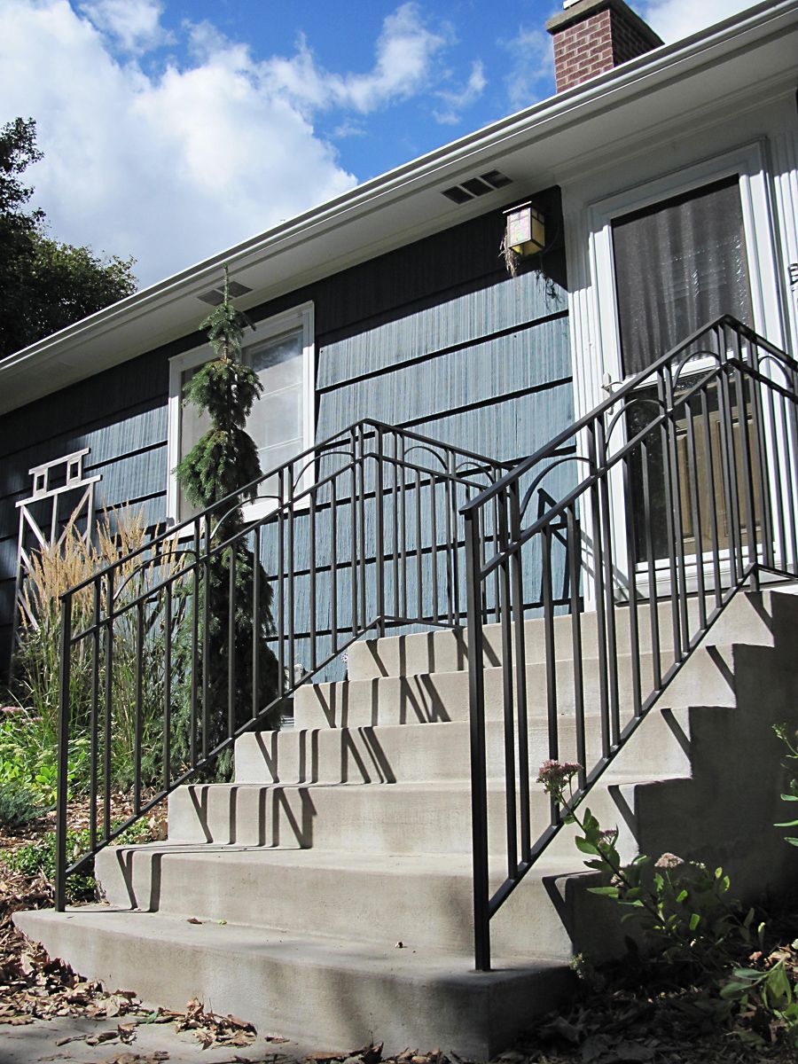 Concrete steps with black metal railing leading to a house with blue siding.