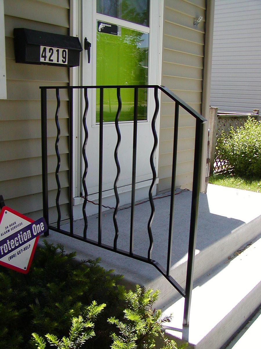 Black metal handrail next to house entrance with decorative wavy vertical bars.