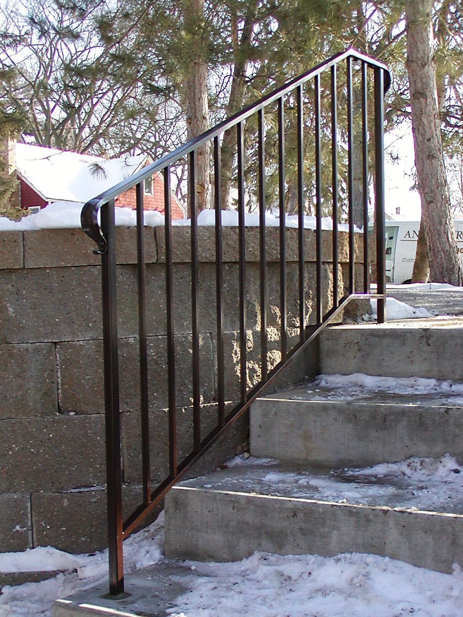 Black metal handrail on concrete steps with winter snow.