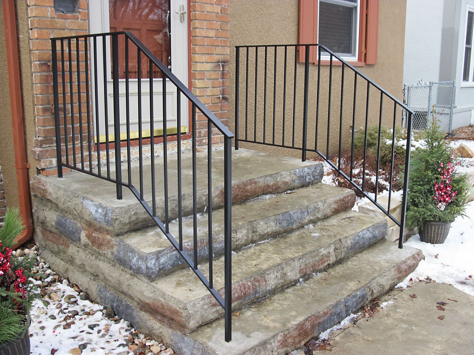 Black metal handrails on concrete steps leading to a front door.
