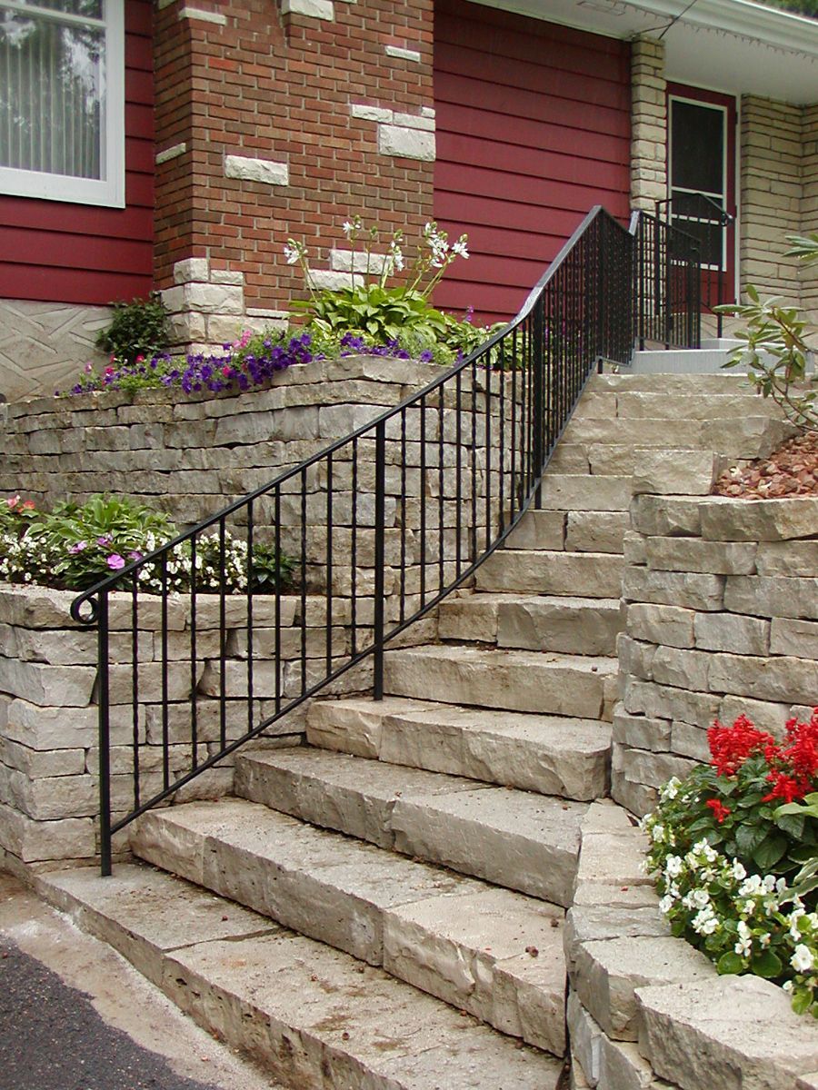 Stone steps with black railing leading to a red and beige home. Landscaping with flowers.