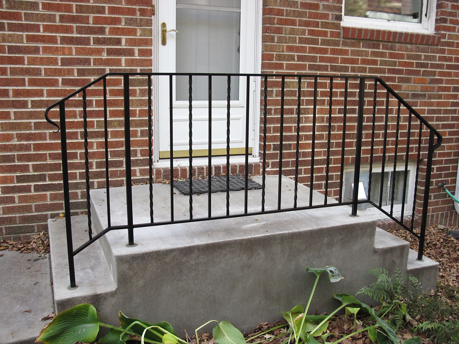 Black metal handrail on concrete steps leading to a brick building's entrance.