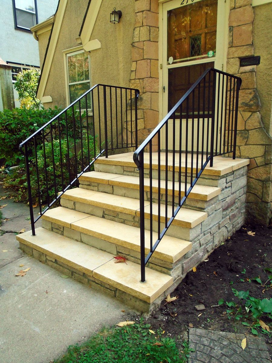 Stone steps leading to a house entrance, with black metal railings.