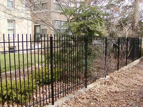 A black wrought iron fence surrounds a lush green yard.