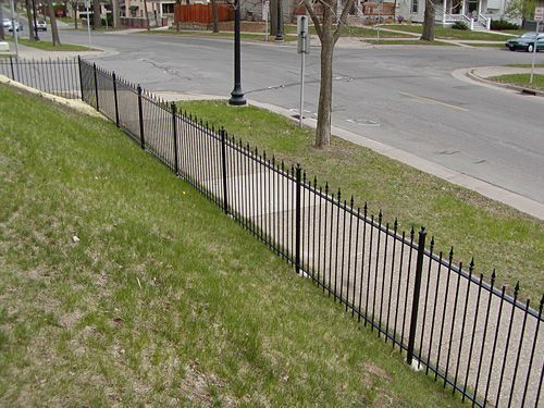 A black wrought iron fence surrounds a grassy area next to a street.