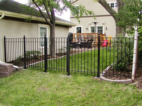 A black fence surrounds a lush green yard in front of a house.
