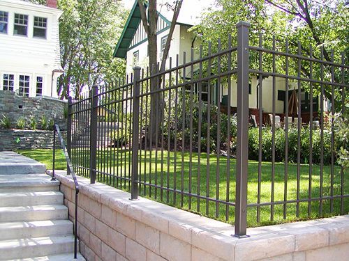 A wrought iron fence surrounds a brick wall in front of a house