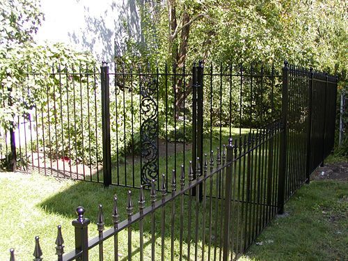 A black wrought iron fence surrounds a lush green yard.