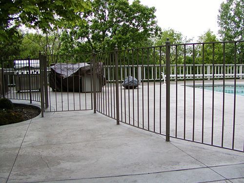 A metal fence surrounds a swimming pool with trees in the background