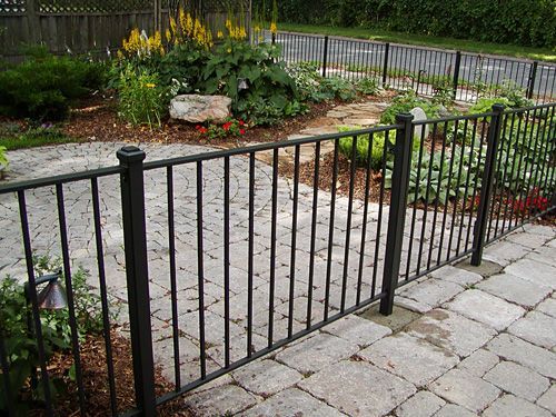A black wrought iron fence surrounds a patio with flowers in the background.