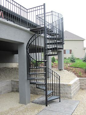 A spiral staircase leading up to a balcony with a house in the background