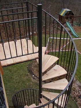 A spiral staircase with wooden steps and a metal railing in a backyard.