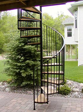 A spiral staircase is sitting on a brick patio in front of a house.