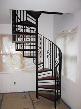 A spiral staircase is sitting in a room next to a window.
