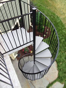 A spiral staircase with a black railing is outside of a house.