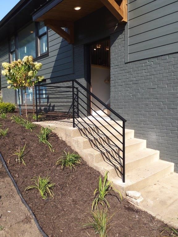 Black metal railing beside concrete steps leading to a gray building entrance.