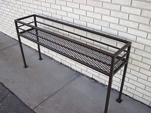 A metal shelf is sitting on a sidewalk in front of a white brick wall.