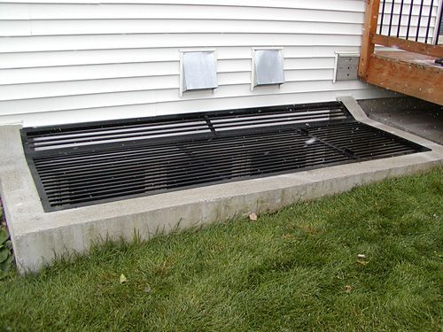 A window well with a metal grate on the side of a house.
