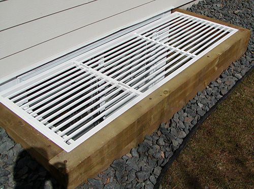 A white window well cover with a wooden frame is sitting on the ground next to a house.