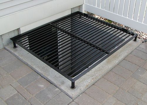 A black metal grate is sitting on a brick sidewalk next to a house.