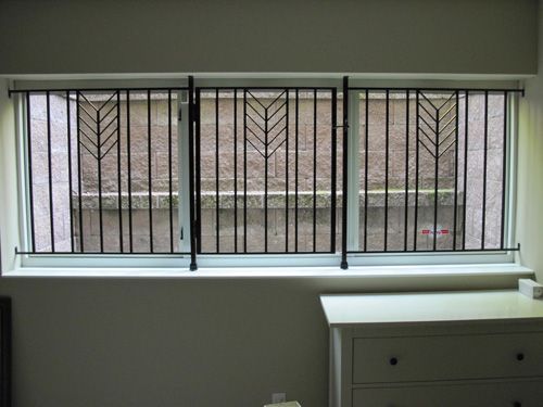 A window with a wrought iron fence and a white dresser in a room.