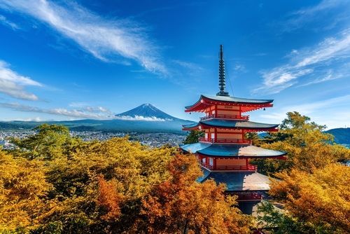 Red pagoda with Mount Fuji in the background, surrounded by autumn foliage under a blue sky.