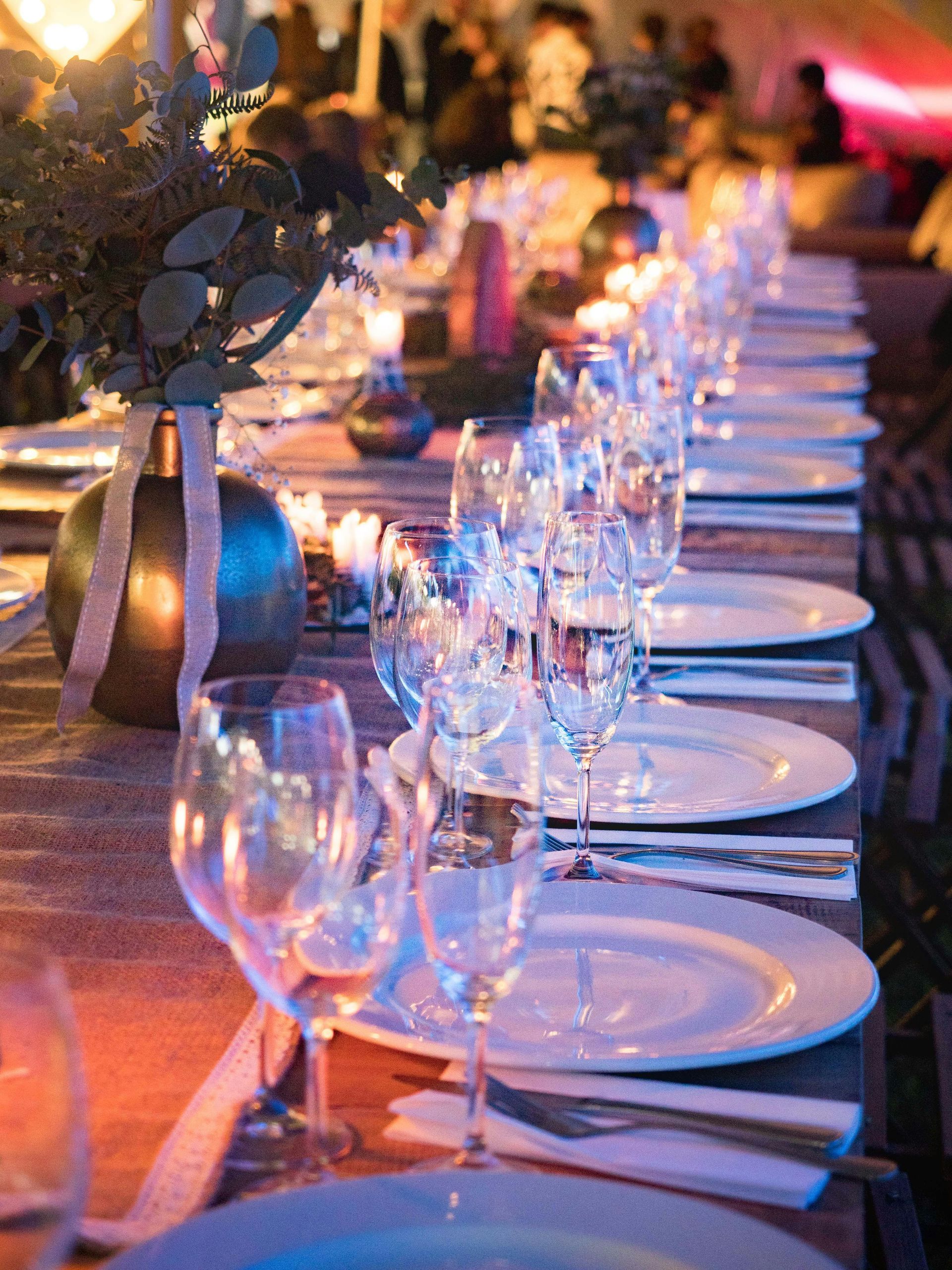 Long table set for a formal event with glassware, white plates, silverware, and decorations.