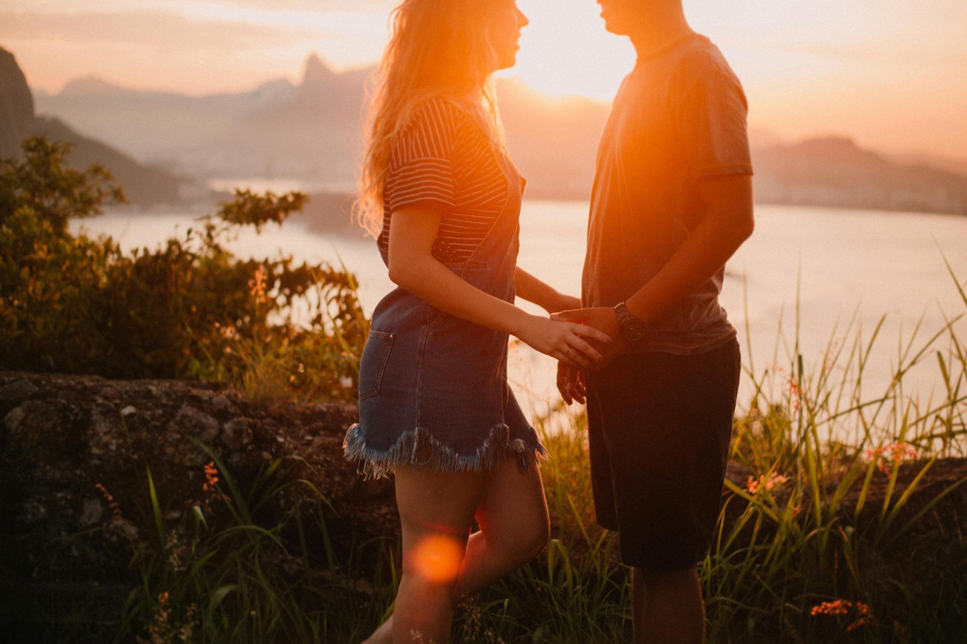 Couple holding hands at sunset, with a mountain and water view.