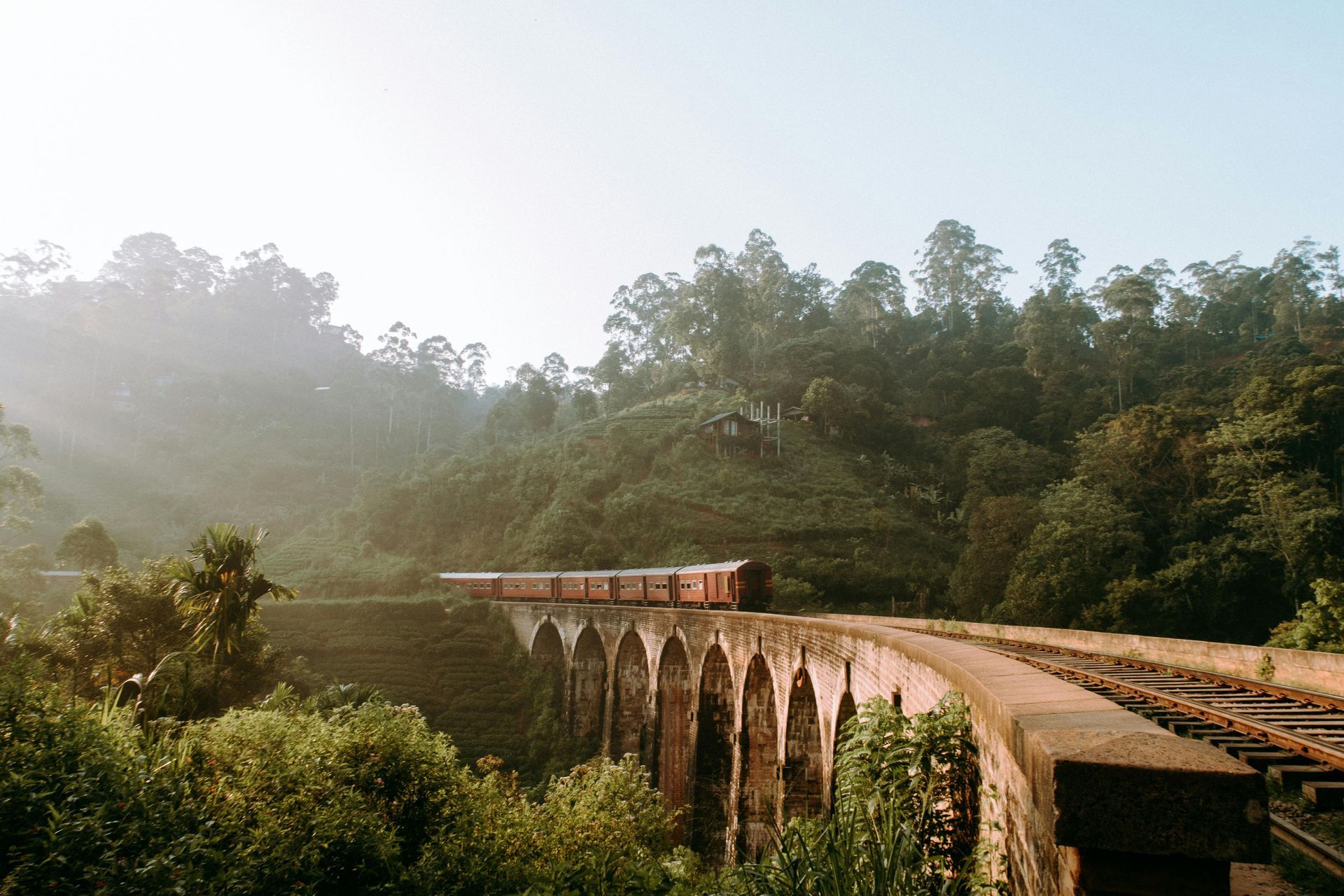 Train crossing the Nine Arch Bridge in Sri Lanka; lush green hills surround the stone bridge.