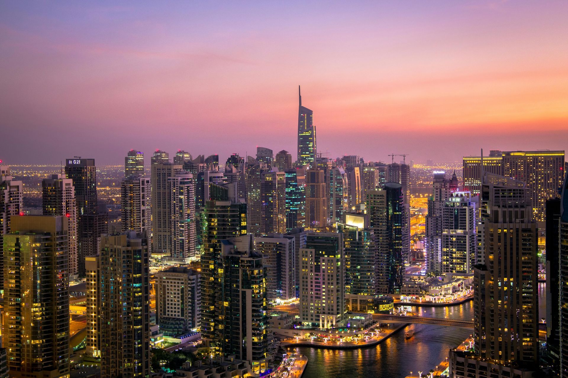 Dubai skyline at sunset with tall illuminated buildings and purple sky.