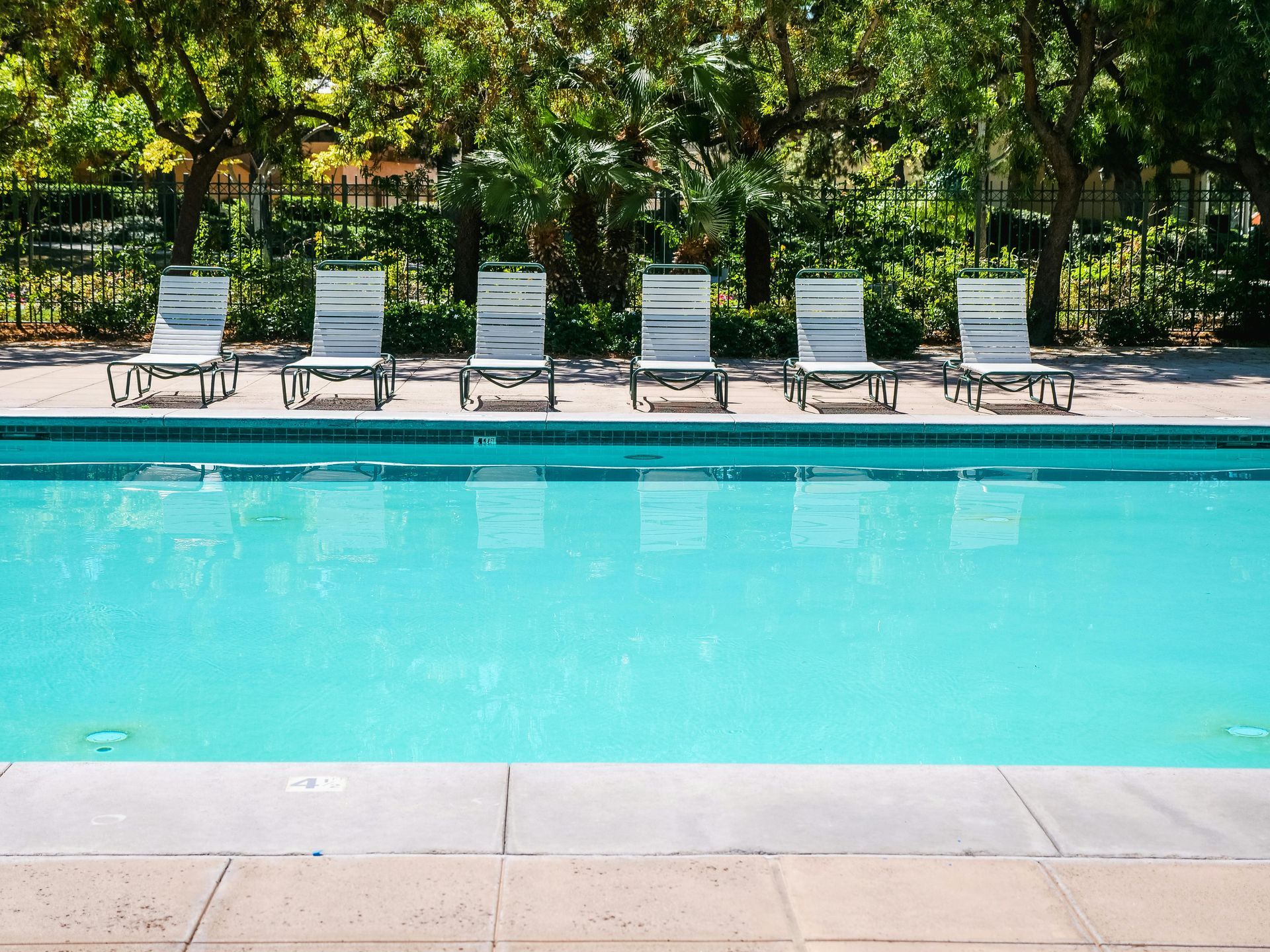 Swimming pool with six white lounge chairs, surrounded by trees.
