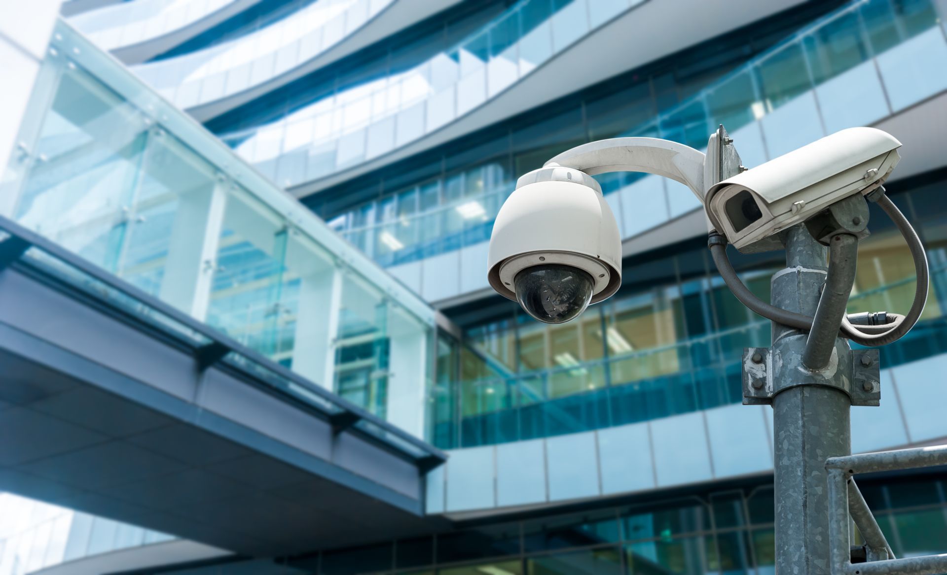 Due telecamere di sicurezza montate su un palo, di fronte a un moderno edificio con pareti in vetro.