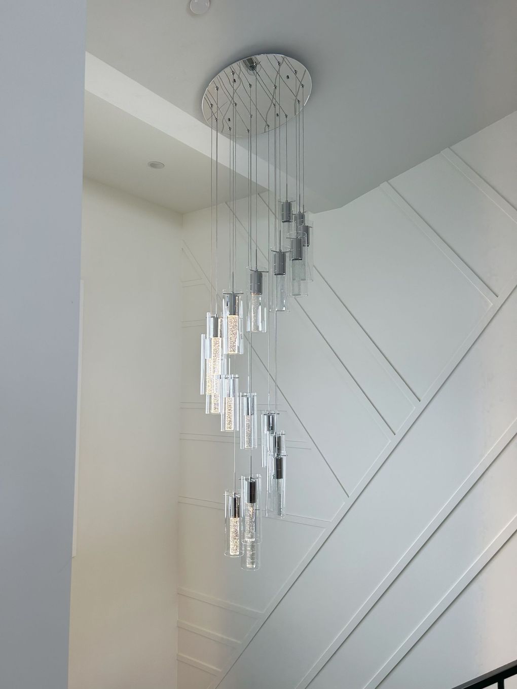 A long chandelier is hanging from the ceiling above a staircase.