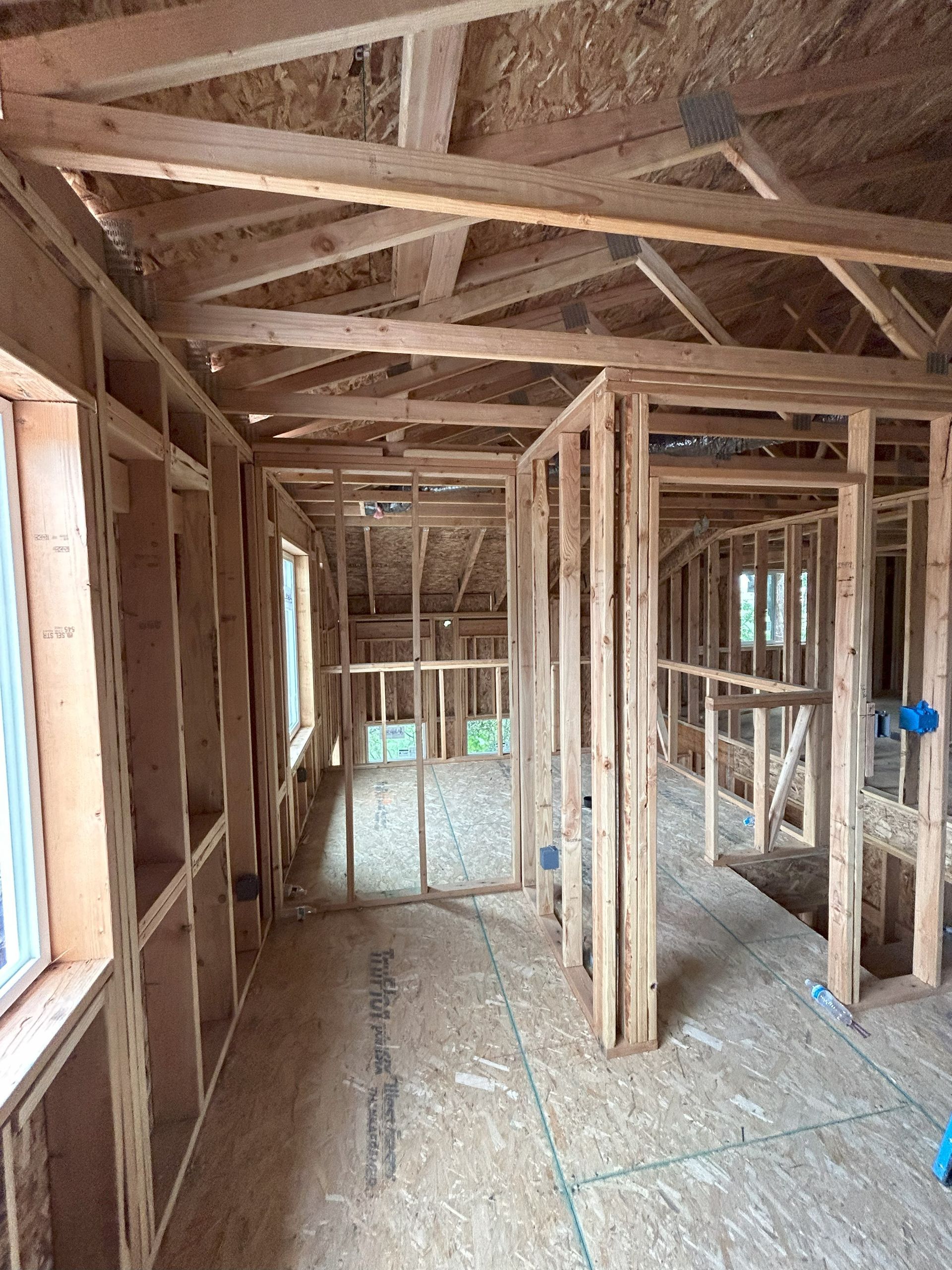 The inside of a house under construction with wooden beams and windows.