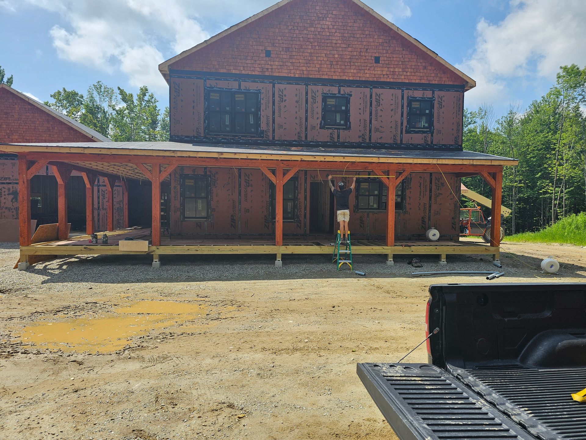 Construction site with a two-story house. A man stands on a ladder near a wooden porch.