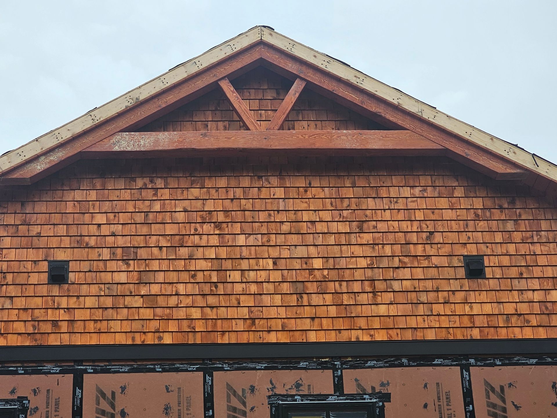Wooden shingle siding on a gable, with a decorative wooden triangle and two square vents.