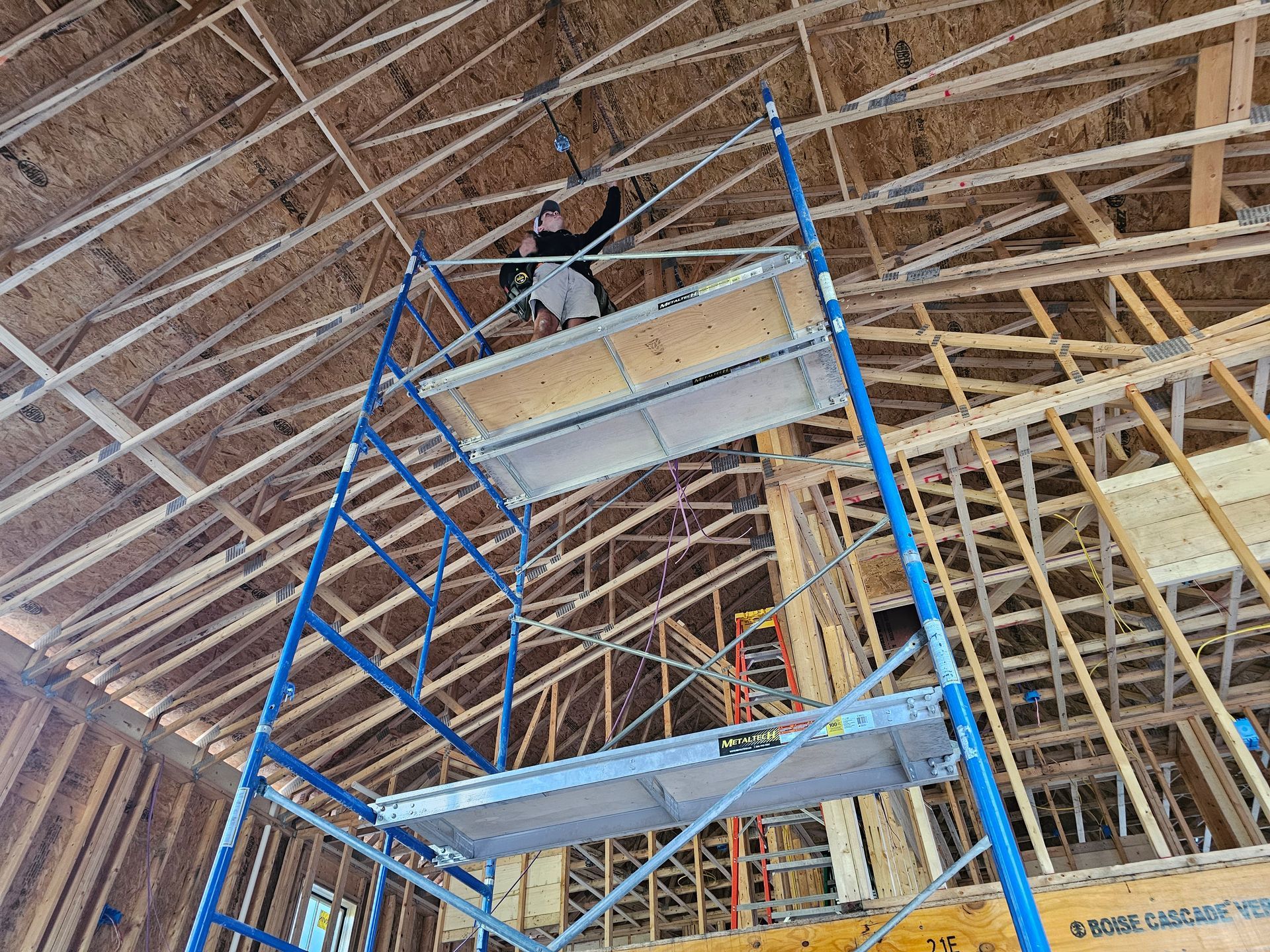 Person on scaffolding working on ceiling construction. Wooden rafters and beams visible.