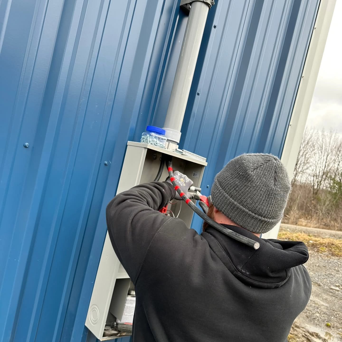 Electrician working on electrical box mounted on blue metal building.