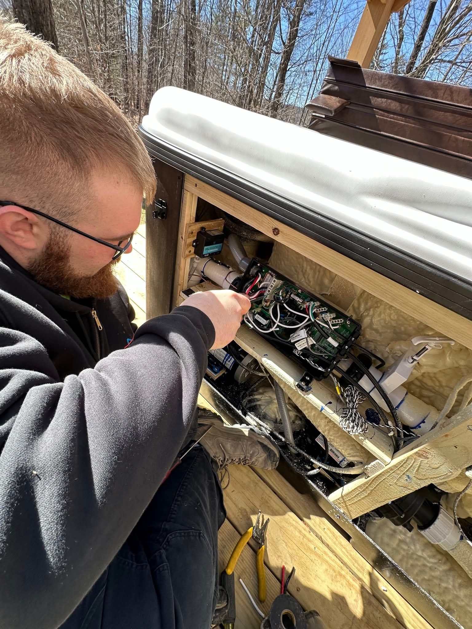 Man working on the electrical components inside a hot tub. Outdoors, sunny.