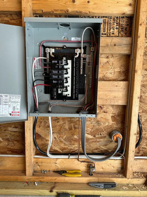 Electrical panel mounted on wooden framing, with wires and breakers visible. Tools are beneath it.