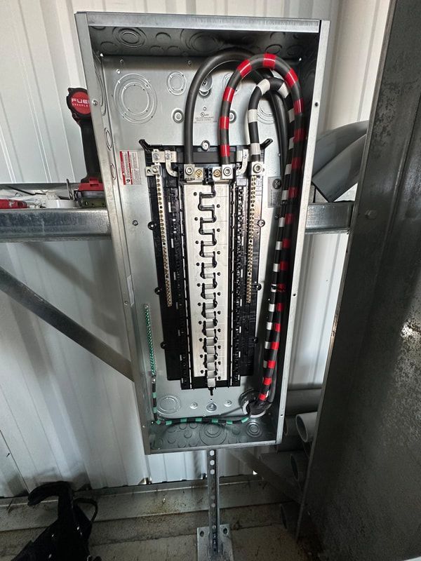 Electrical panel with connected wires, mounted on a wall. Red, black, and white wires visible.