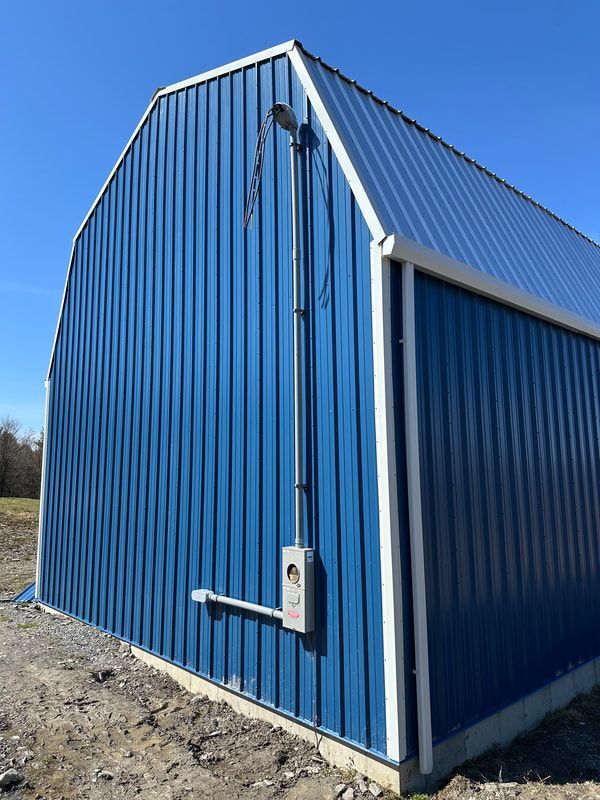 Blue metal barn with white trim and electrical conduit against a clear blue sky.