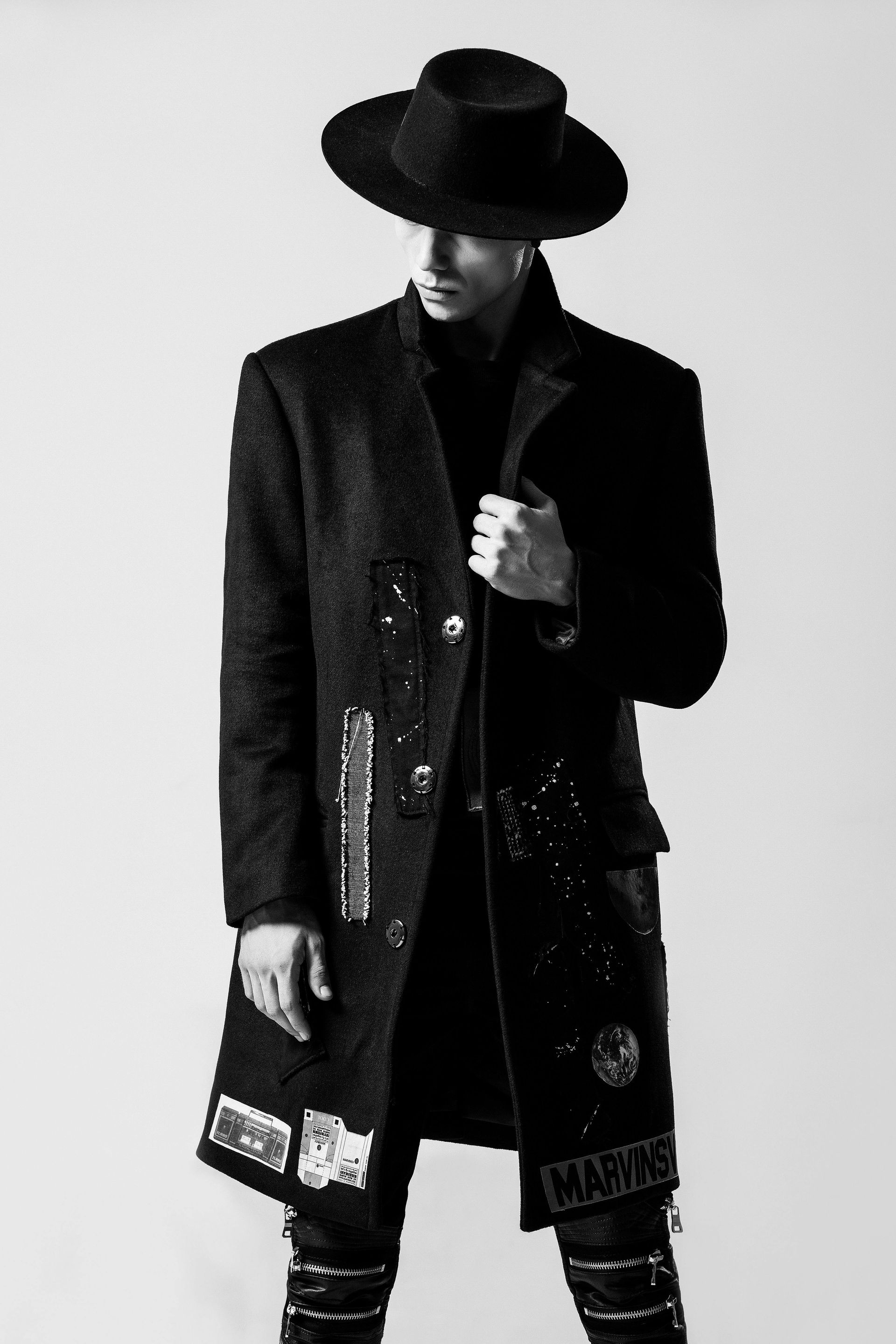 Person in black coat and hat, holding jacket. Black and white photo.