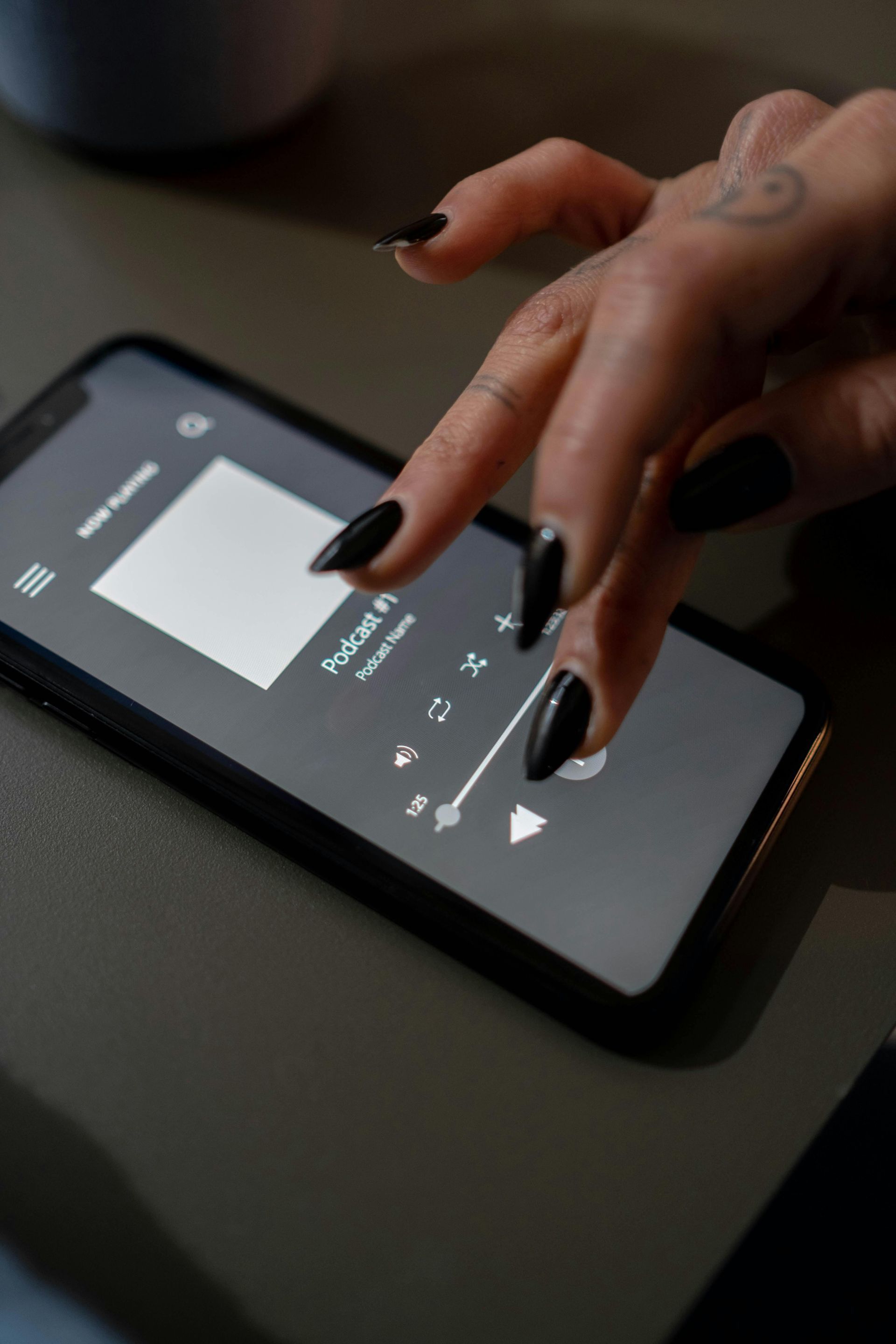 Person with black nail polish using a phone with a music player interface on a dark surface.