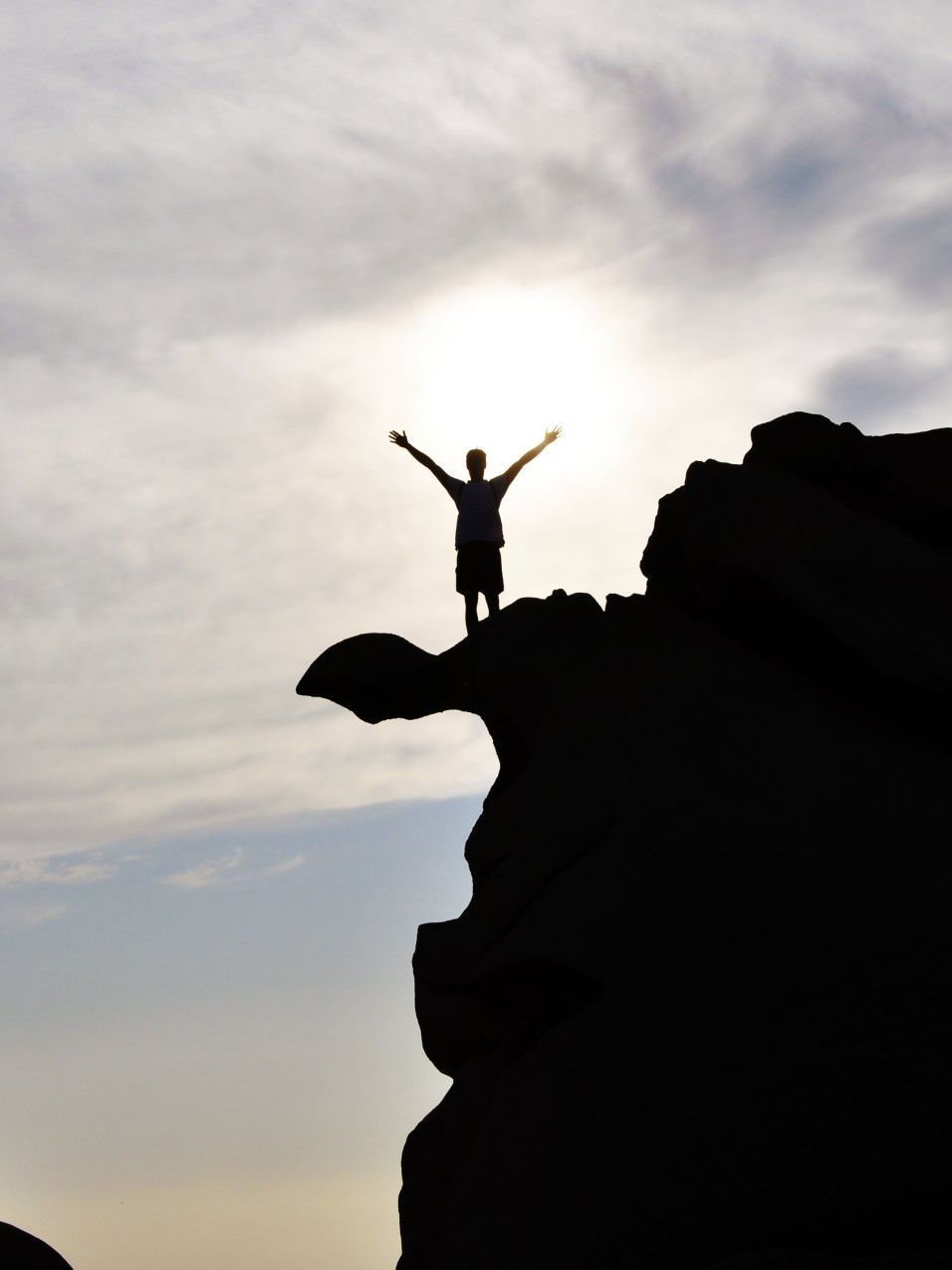 A silhouette of a person standing on a cliff with their arms outstretched